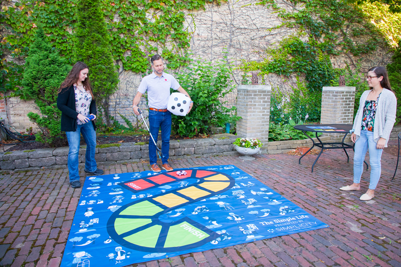 Three people standing on a brick patio playing a game
